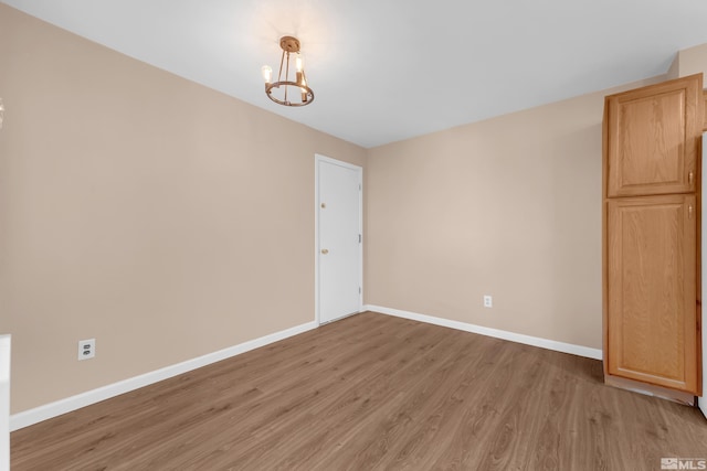 empty room featuring a chandelier and light wood-type flooring