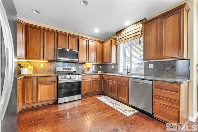 kitchen with decorative backsplash, stainless steel appliances, dark wood-type flooring, sink, and dark stone countertops