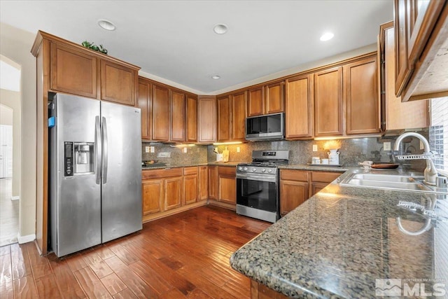 kitchen with decorative backsplash, appliances with stainless steel finishes, dark hardwood / wood-style flooring, sink, and stone counters