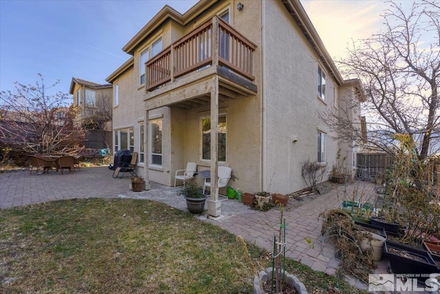 property exterior at dusk featuring a lawn, a balcony, and a patio