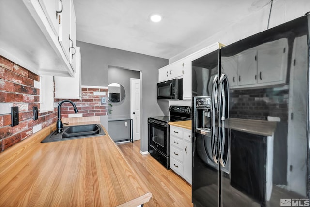 kitchen featuring black appliances, white cabinets, light wood-type flooring, and sink