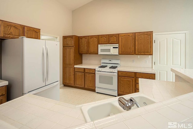 kitchen featuring white appliances, tile countertops, high vaulted ceiling, and sink