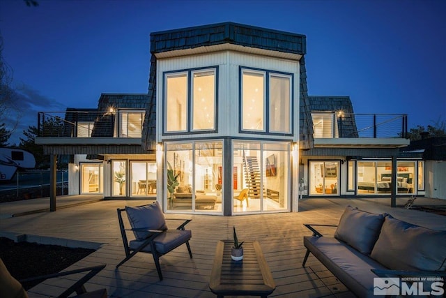 back house at night with outdoor lounge area and a deck