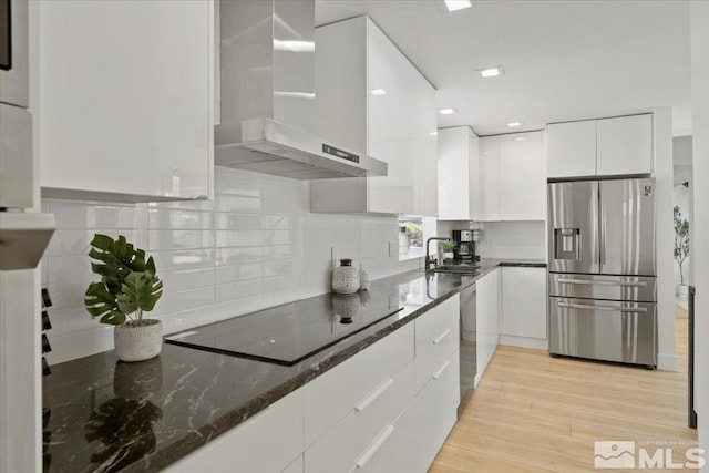 kitchen featuring dark stone counters, wall chimney exhaust hood, light wood-type flooring, white cabinetry, and stainless steel appliances