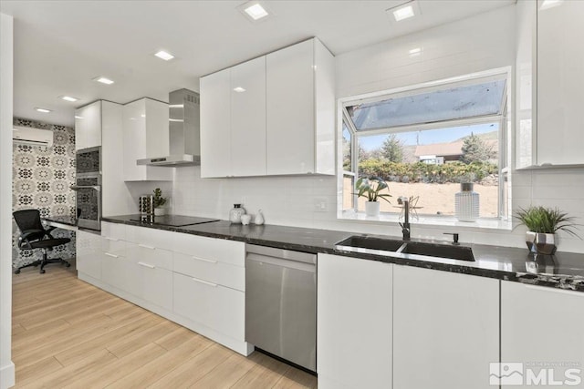 kitchen with stainless steel dishwasher, wall chimney exhaust hood, sink, white cabinets, and light hardwood / wood-style floors