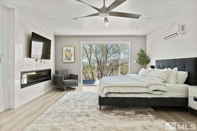 bedroom featuring an AC wall unit, a tile fireplace, ceiling fan, and light hardwood / wood-style floors