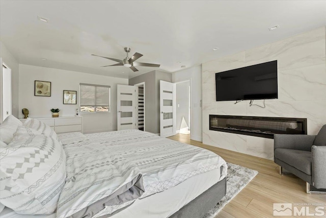 bedroom with light wood-type flooring, ceiling fan, and a premium fireplace