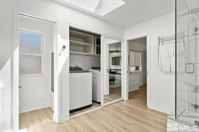 clothes washing area featuring washer and dryer, light wood-type flooring, and a skylight