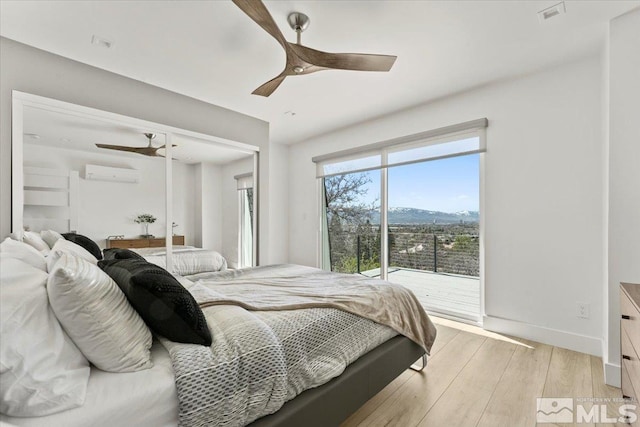 bedroom with a mountain view, an AC wall unit, ceiling fan, access to exterior, and light wood-type flooring