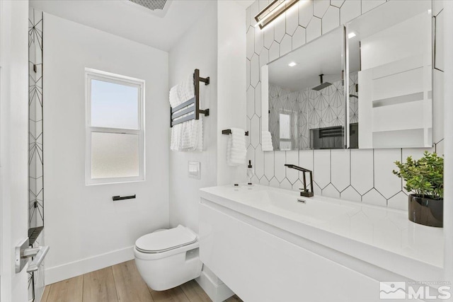 bathroom featuring hardwood / wood-style floors, vanity, backsplash, toilet, and a tile shower