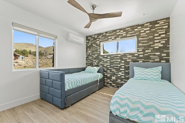 bedroom featuring a mountain view, an AC wall unit, light hardwood / wood-style flooring, ceiling fan, and tile walls