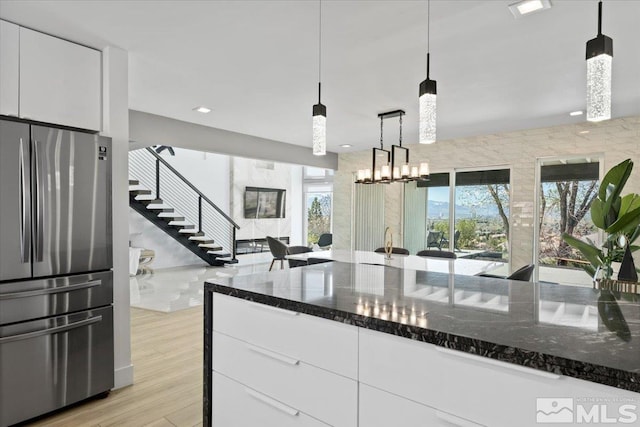 kitchen featuring decorative light fixtures, stainless steel fridge, dark stone countertops, and white cabinetry