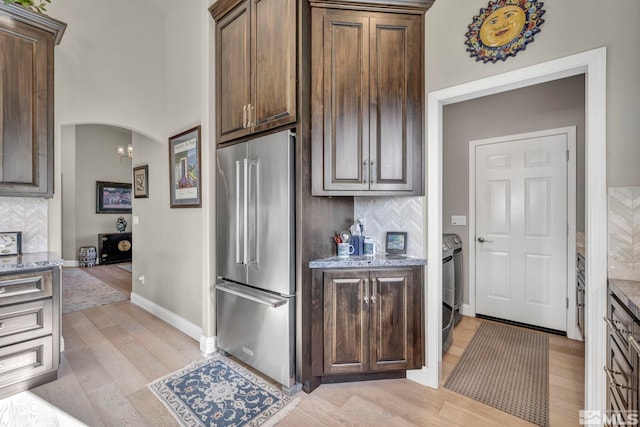 kitchen with light wood-type flooring, tasteful backsplash, light stone counters, high end fridge, and dark brown cabinetry