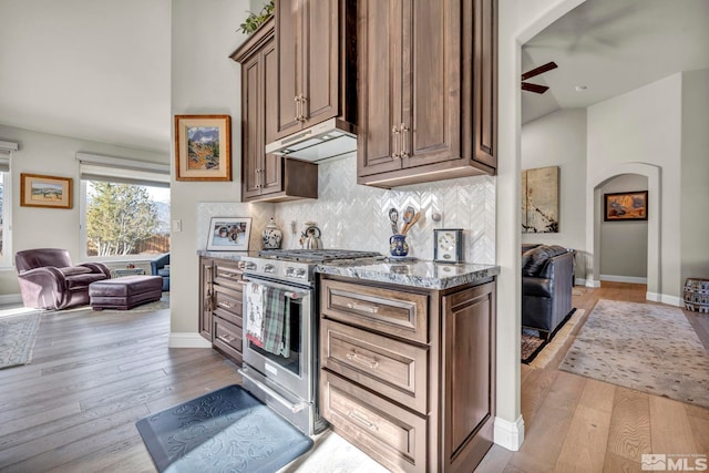 kitchen with ceiling fan, stainless steel range, light hardwood / wood-style flooring, backsplash, and dark stone counters