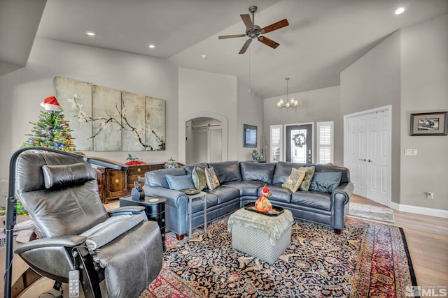 living room with ceiling fan with notable chandelier, light wood-type flooring, and high vaulted ceiling