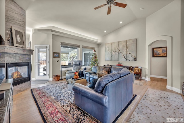 living room with light hardwood / wood-style floors, high vaulted ceiling, ceiling fan, and a tiled fireplace