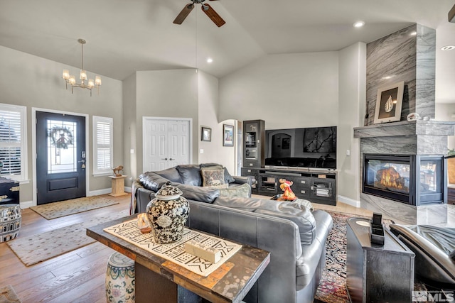 living room featuring ceiling fan with notable chandelier, light wood-type flooring, high vaulted ceiling, and a tiled fireplace