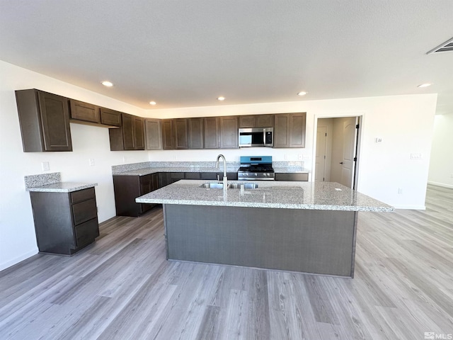 kitchen featuring an island with sink, sink, appliances with stainless steel finishes, and light hardwood / wood-style flooring