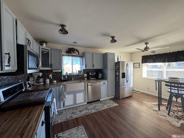 kitchen with ceiling fan, dark wood-type flooring, wooden counters, backsplash, and appliances with stainless steel finishes