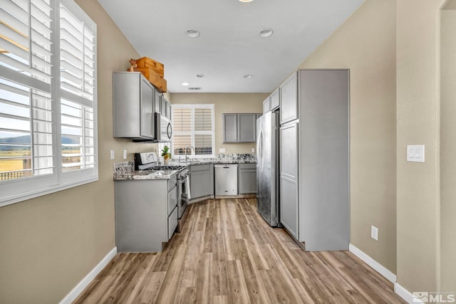 kitchen featuring gray cabinetry, light stone countertops, sink, appliances with stainless steel finishes, and light wood-type flooring