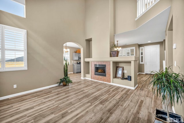 unfurnished living room with a tiled fireplace, a chandelier, a high ceiling, and hardwood / wood-style flooring