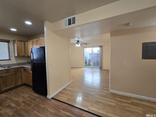 kitchen featuring hardwood / wood-style floors, electric panel, black refrigerator, sink, and ceiling fan