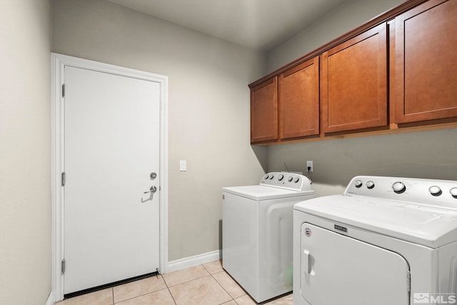 clothes washing area with washing machine and dryer, light tile patterned floors, and cabinets