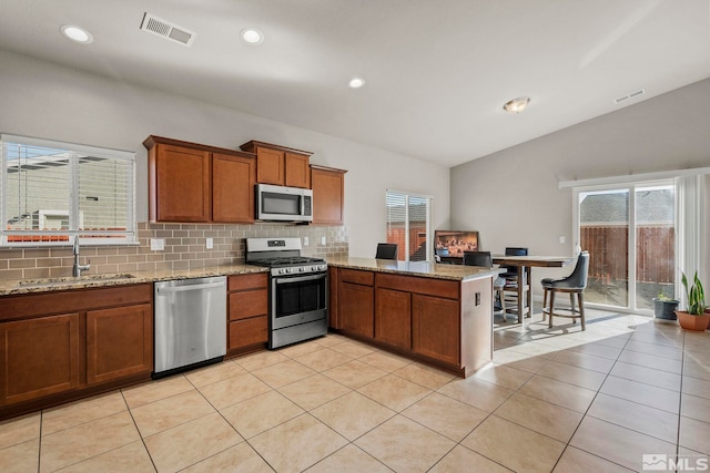 kitchen with kitchen peninsula, appliances with stainless steel finishes, light stone countertops, sink, and lofted ceiling