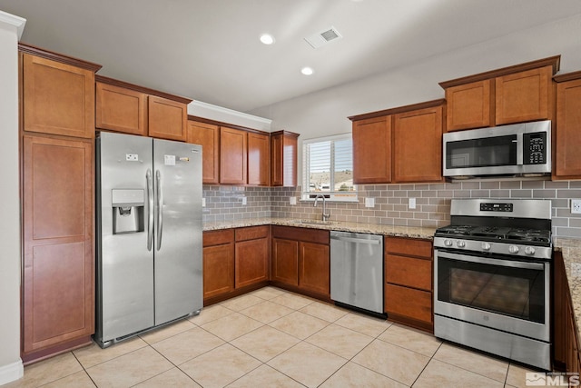 kitchen with light stone countertops, appliances with stainless steel finishes, tasteful backsplash, sink, and light tile patterned flooring