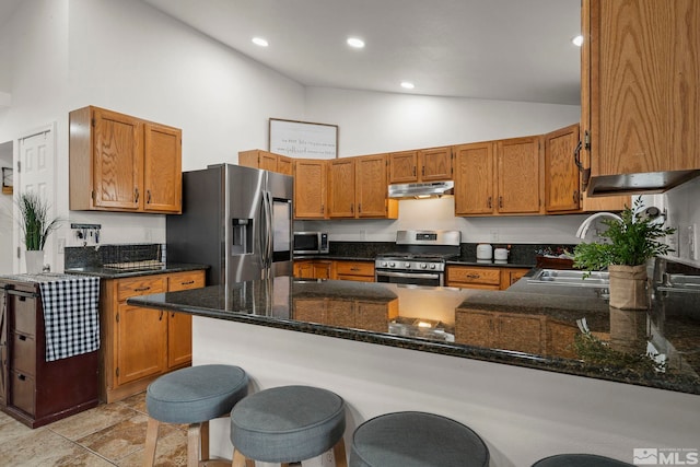 kitchen with a kitchen breakfast bar, kitchen peninsula, appliances with stainless steel finishes, and dark stone counters