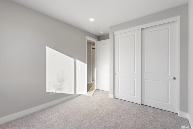 unfurnished bedroom featuring light carpet, a closet, and baseboards