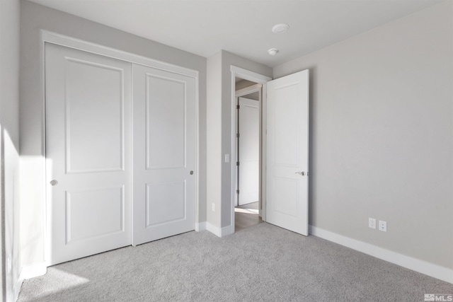 unfurnished bedroom featuring a closet, light carpet, and baseboards