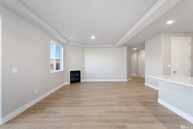 unfurnished living room featuring recessed lighting, visible vents, a glass covered fireplace, light wood-type flooring, and baseboards