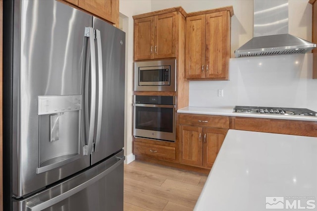 kitchen featuring appliances with stainless steel finishes, light hardwood / wood-style floors, and wall chimney range hood