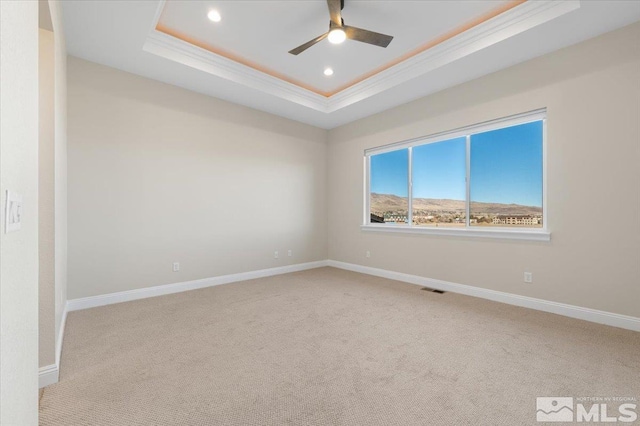 empty room with a tray ceiling, ceiling fan, light colored carpet, and ornamental molding