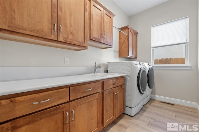 clothes washing area with cabinets, separate washer and dryer, light hardwood / wood-style flooring, and sink