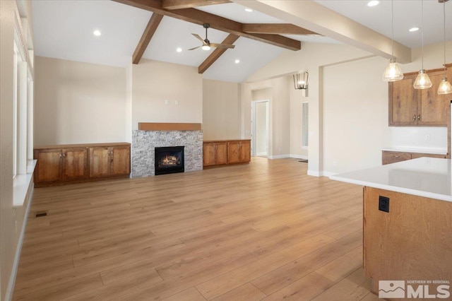 unfurnished living room with a fireplace, lofted ceiling with beams, light hardwood / wood-style floors, and ceiling fan