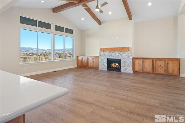 unfurnished living room with a mountain view, high vaulted ceiling, a stone fireplace, beamed ceiling, and light hardwood / wood-style floors