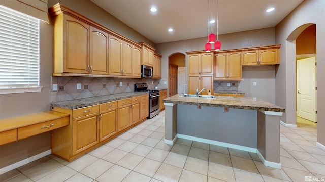 kitchen featuring light stone countertops, appliances with stainless steel finishes, backsplash, sink, and a center island with sink