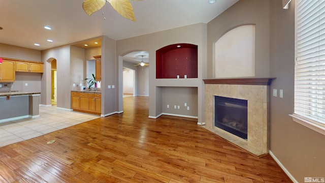 unfurnished living room featuring ceiling fan, a tiled fireplace, and light hardwood / wood-style flooring