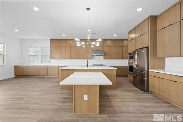 kitchen featuring sink, a center island with sink, an inviting chandelier, light hardwood / wood-style flooring, and stainless steel refrigerator