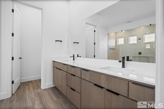 bathroom featuring a tile shower, vanity, and wood-type flooring