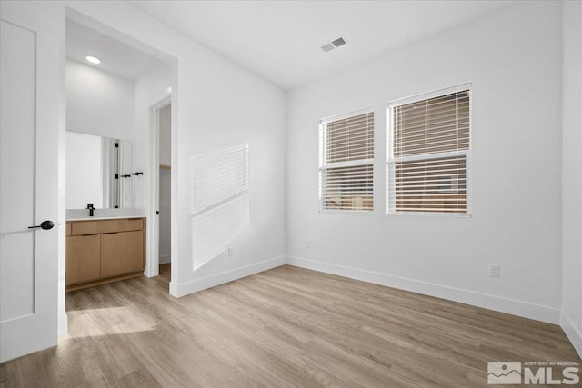 unfurnished bedroom with ensuite bathroom, sink, and light wood-type flooring