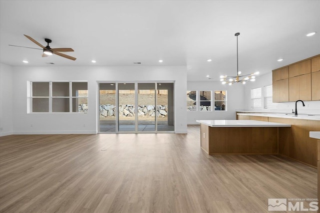 kitchen featuring sink, hanging light fixtures, ceiling fan with notable chandelier, and light wood-type flooring