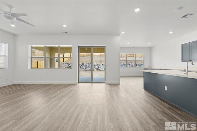 unfurnished living room with light hardwood / wood-style floors, ceiling fan, and sink