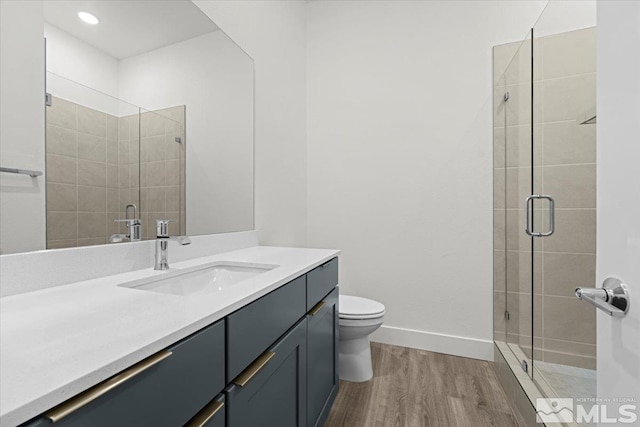 bathroom with wood-type flooring, vanity, toilet, and a shower with shower door