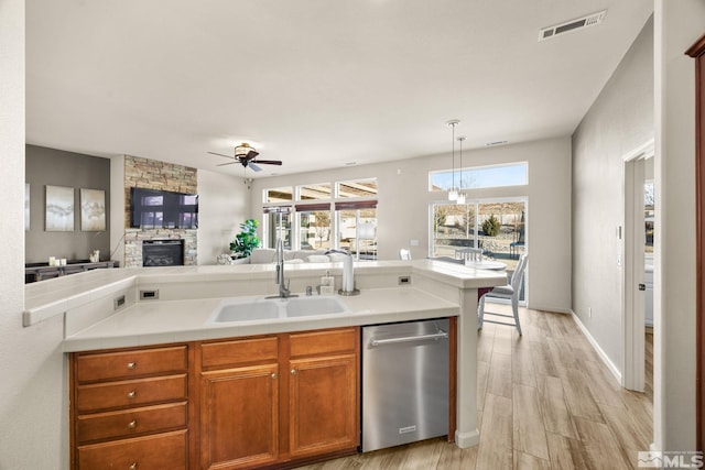 kitchen featuring sink, a stone fireplace, light hardwood / wood-style flooring, stainless steel dishwasher, and pendant lighting