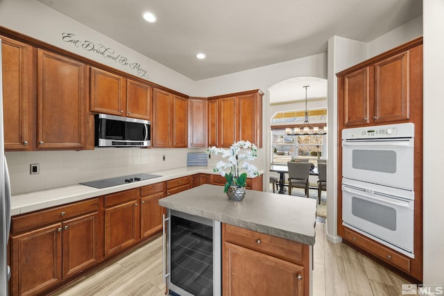 kitchen featuring decorative backsplash, black electric stovetop, white double oven, beverage cooler, and light hardwood / wood-style floors