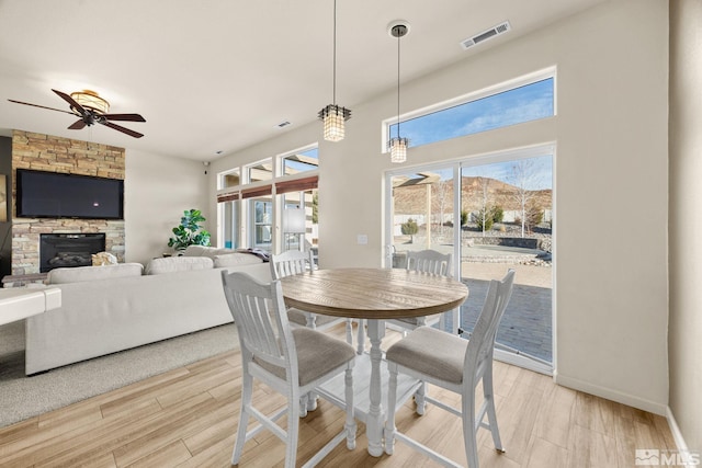 dining room featuring ceiling fan, light hardwood / wood-style floors, and a stone fireplace