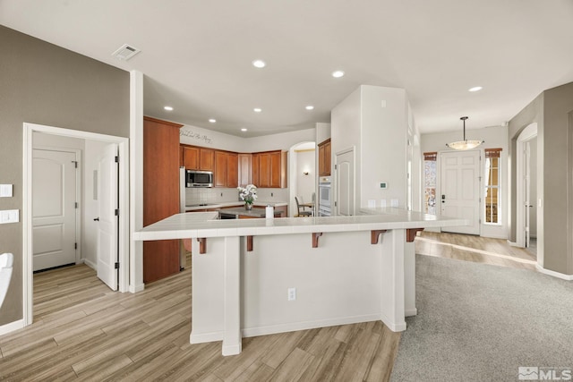 kitchen featuring a breakfast bar, decorative light fixtures, light hardwood / wood-style flooring, tasteful backsplash, and a large island